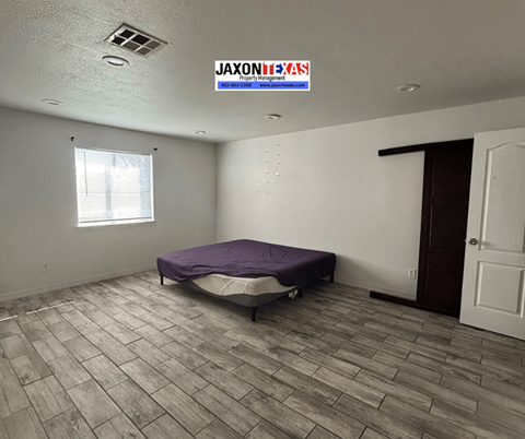 A bedroom with a bed, window, and a JAXON TEXAS sign on the ceiling.