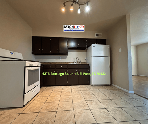 A kitchen with a white refrigerator and black cabinets under a JAXONBYS sign.