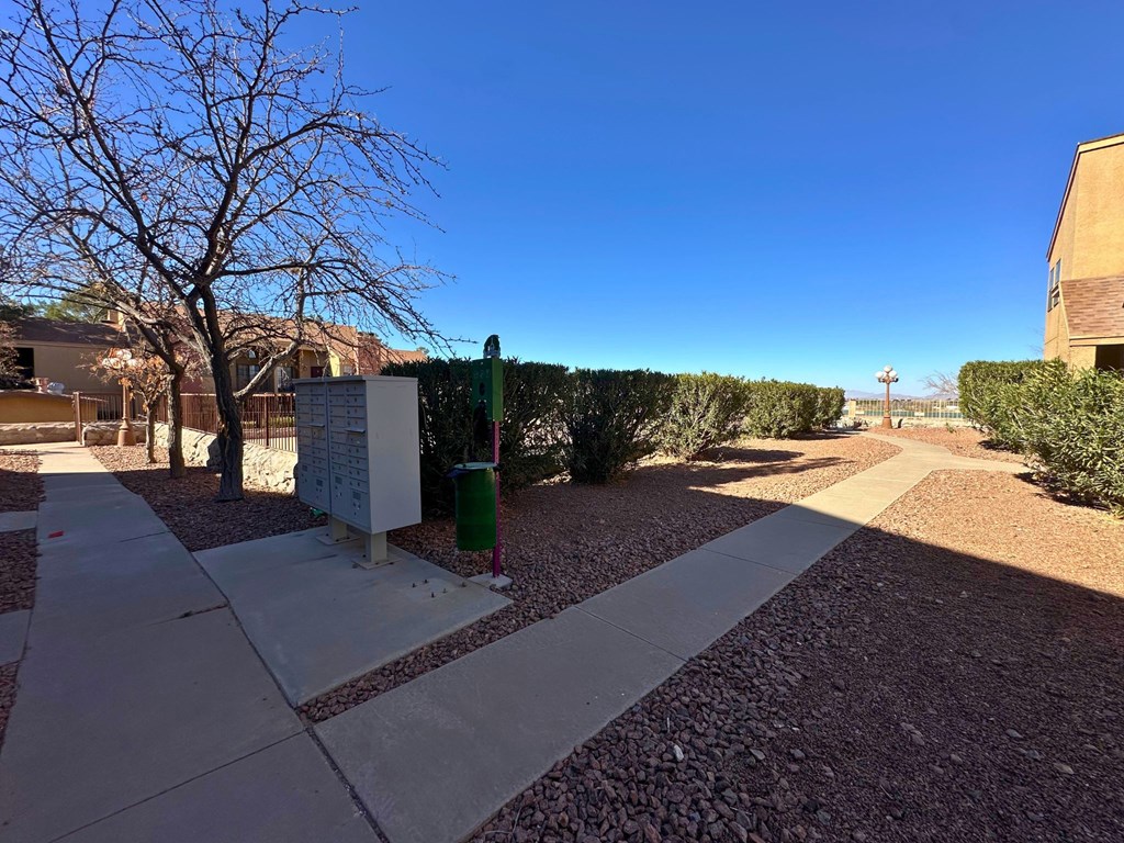 A sunny day in a courtyard with a white pathway, a green trash can, and a white utility box.