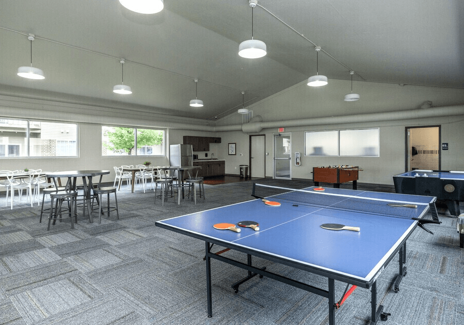 A ping pong table is in the middle of a room with chairs and tables at Courtyard Apartments on Belsly Apartments, Minnesota