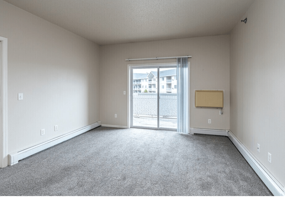 A large empty room with a carpeted floor and a sliding glass door leading to a balcony at Courtyard Apartments on Belsly  Apartments, Moorhead, MN