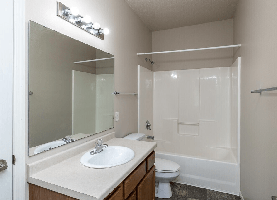 A white bathroom with a sink, mirror, toilet and bathtub at Courtyard Apartments on Belsly Apartments, Minnesota, 56560