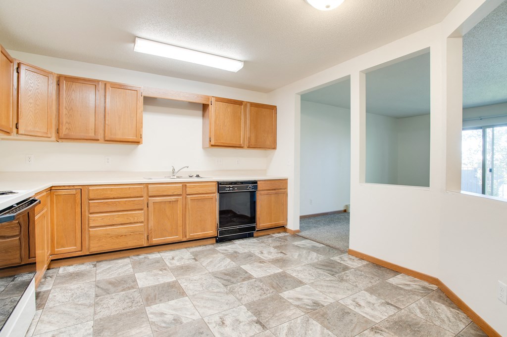 an empty kitchen with wooden cabinets and a black dishwasher, Sandstone Apartments, Fargo, ND, 58103