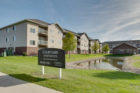 a sign sits in the grass in front of an apartment complex with a pond