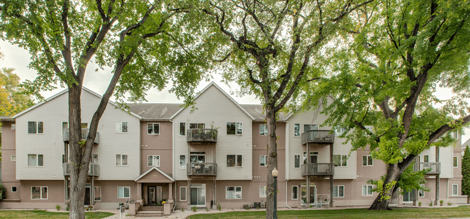 A large apartment building with balconies and trees in front.