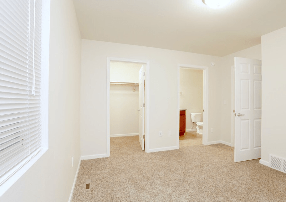 A white room with a carpeted floor and a window with blinds.