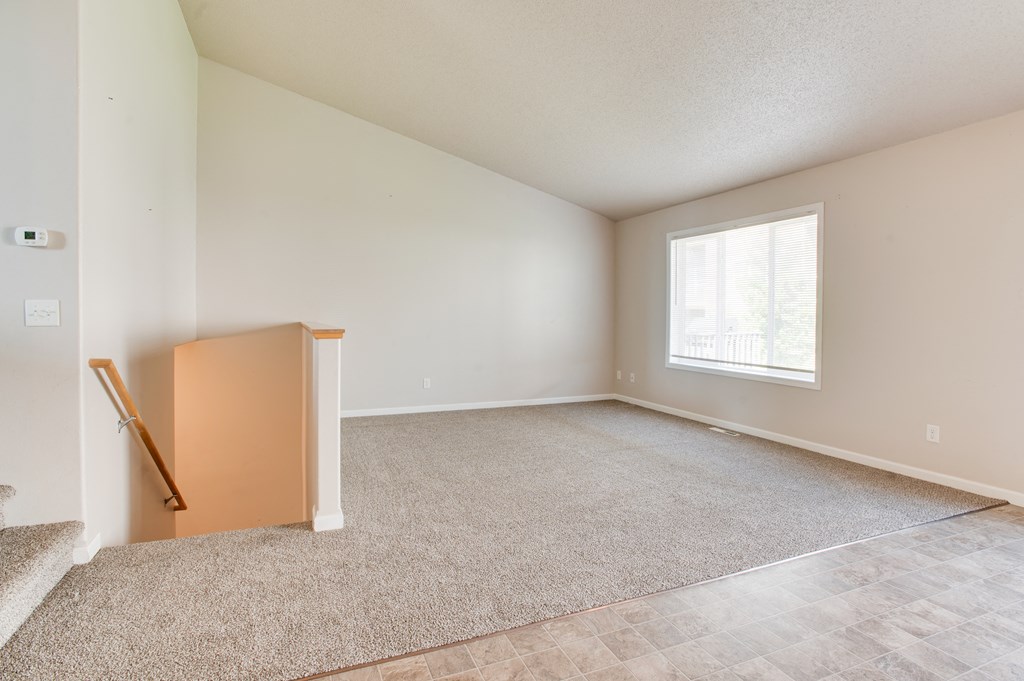 an empty living room with a window and a stairway