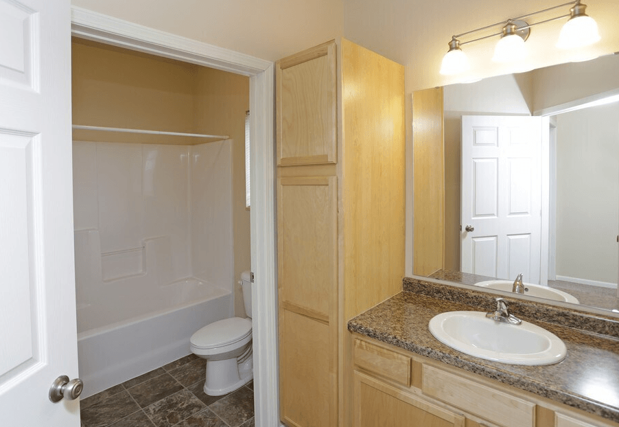 A bathroom with a toilet, sink, and mirror. at Shadow Ridge Apartments, North Dakota