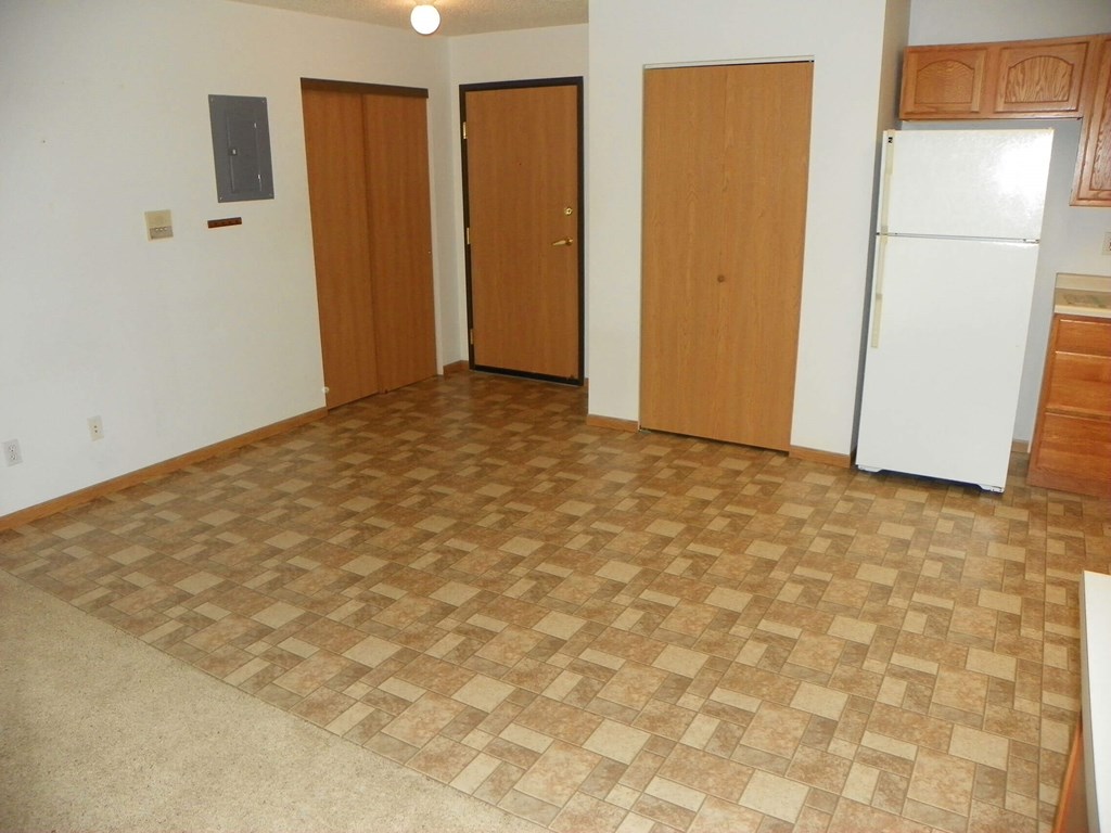 A kitchen with a white fridge and brown flooring.