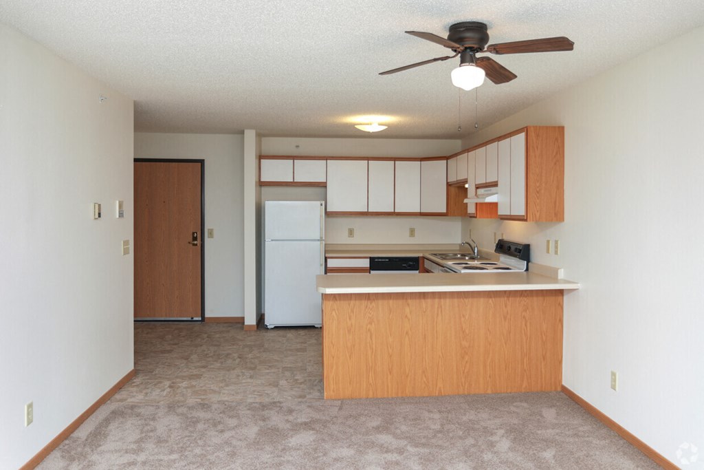 an empty living room with a kitchen and a ceiling fan