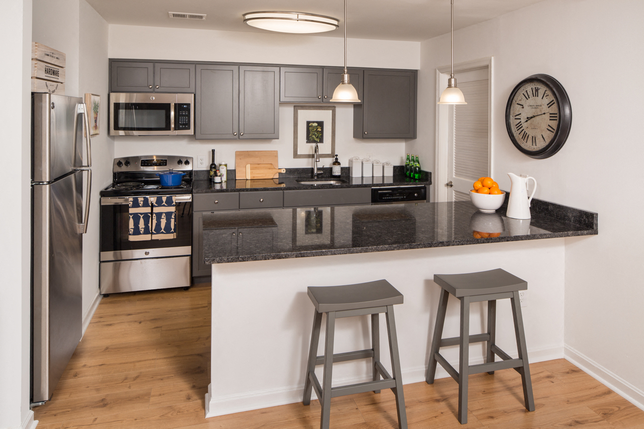 A kitchen with a refrigerator, stove, and bar stools.