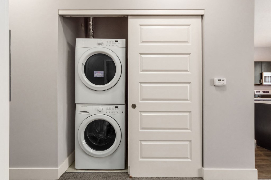 A white door is open to reveal a stacked washer and dryer.