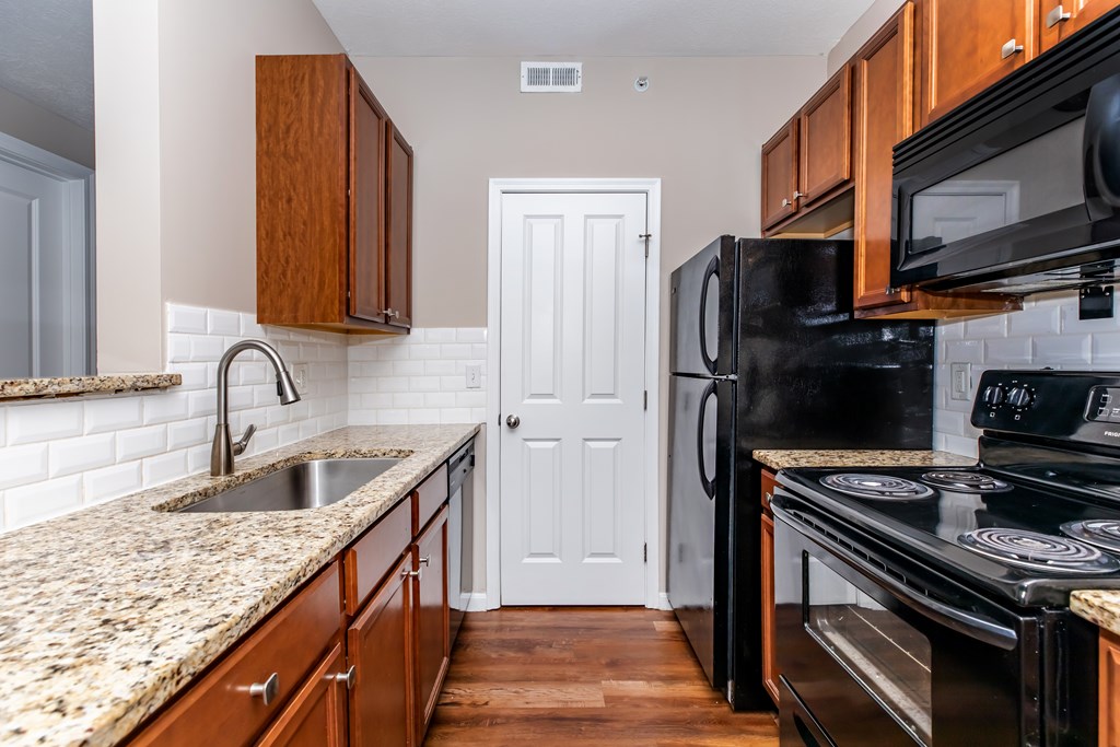 A kitchen with a black refrigerator and stove top oven.