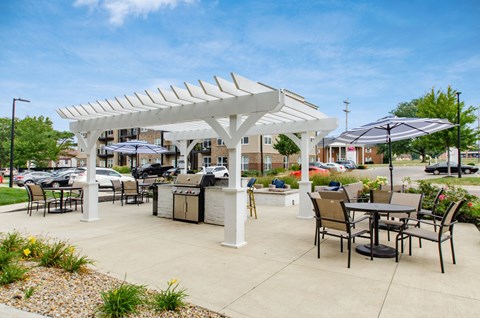 A white pergola with black chairs and tables is set up in a sunny outdoor area.