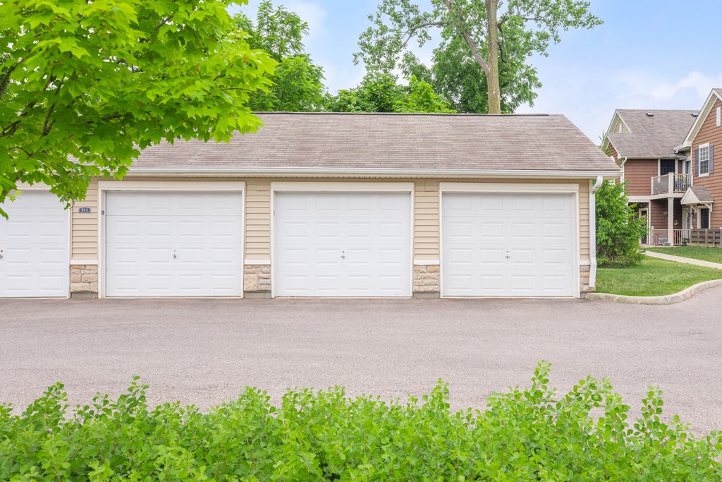 A two-car garage with a brown roof is surrounded by greenery.