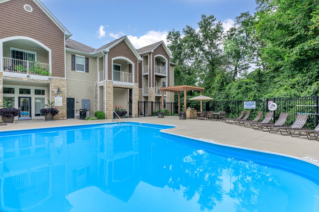 A swimming pool in front of a building with a fence and trees in the background.