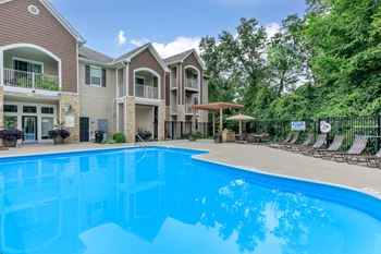 A swimming pool in front of a building with a fence and trees in the background.