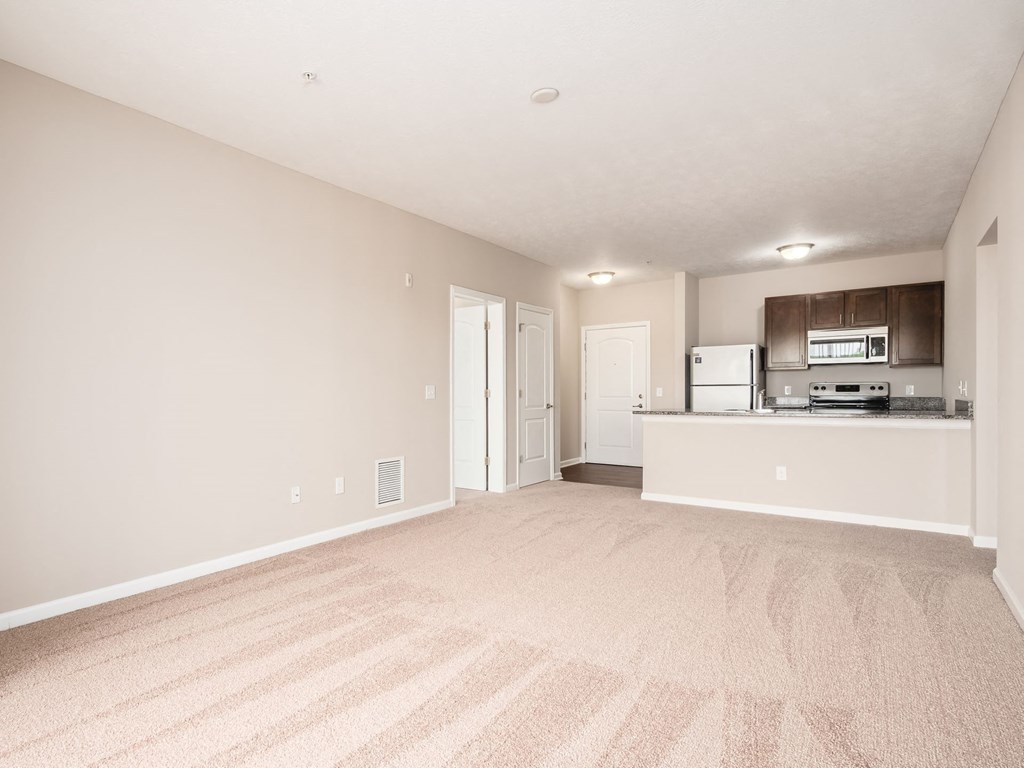 an empty living room with a kitchen with a microwave and refrigerator