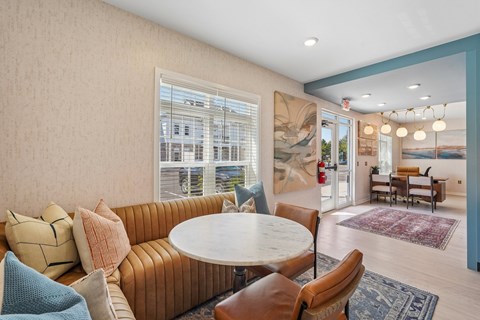 A living room with a round table surrounded by chairs and a large window.