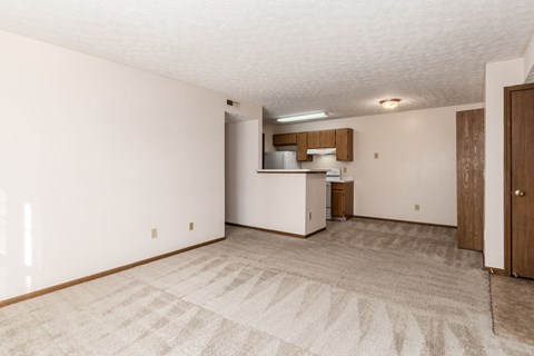 A room with a carpeted floor and a small kitchenette.