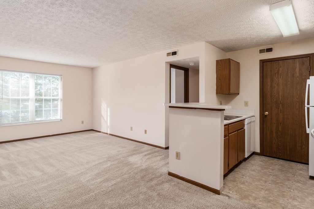 an empty living room and kitchen with a refrigerator and a sink