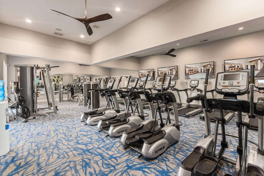 a gym with cardio machines and a ceiling fan