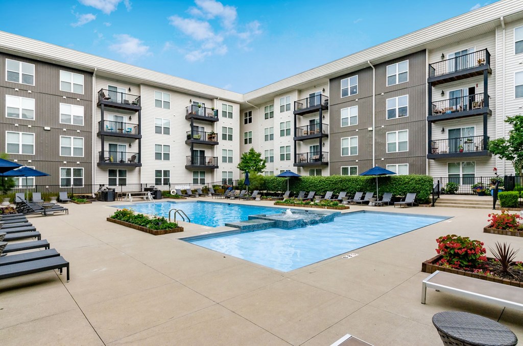 an outdoor pool with lounge chairs and umbrellas in front of an apartment building