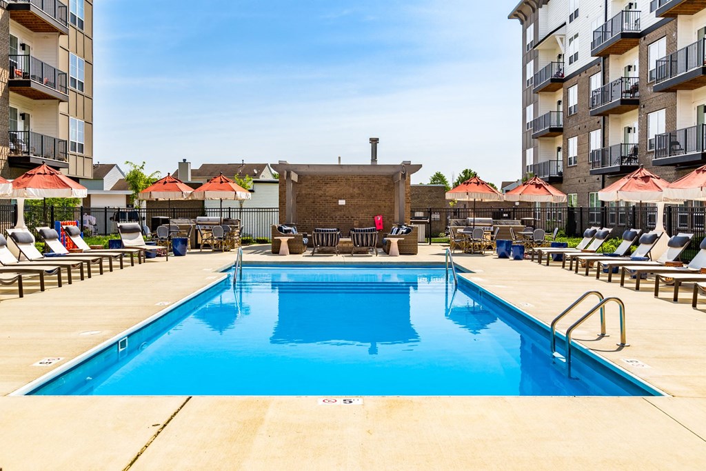 a swimming pool in front of an apartment building with umbrellas
