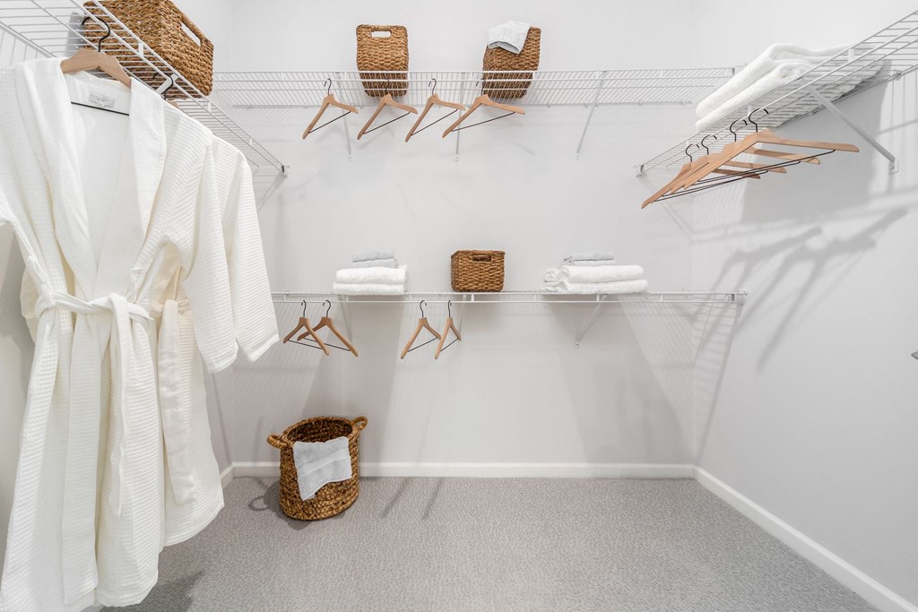 a white walk in closet with white robes and wicker baskets on the racks
