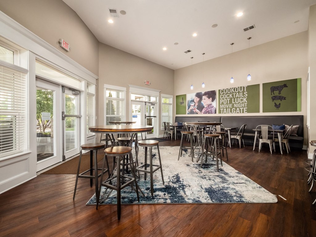 a common room with tables and chairs and a bar and windows