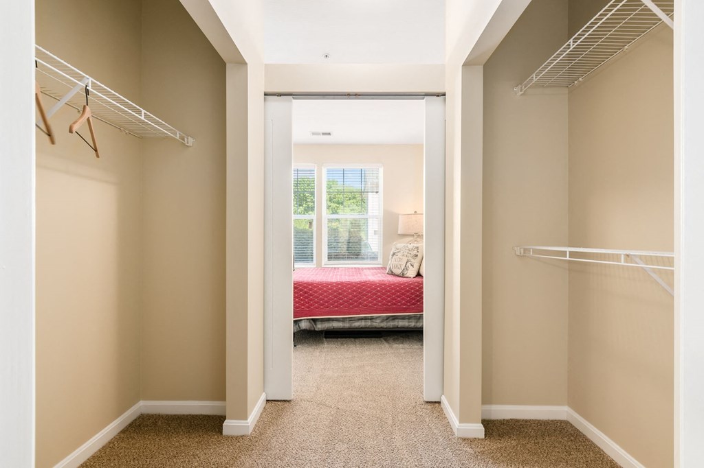a walk in closet with a bed in the background and a mirrored closet door
