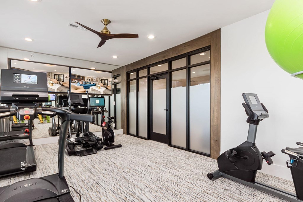a gym with treadmills and other exercise equipment in a room with glass doors