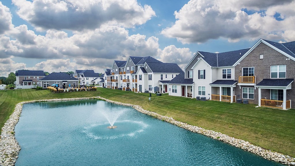 a fountain in the middle of a pond in front of houses