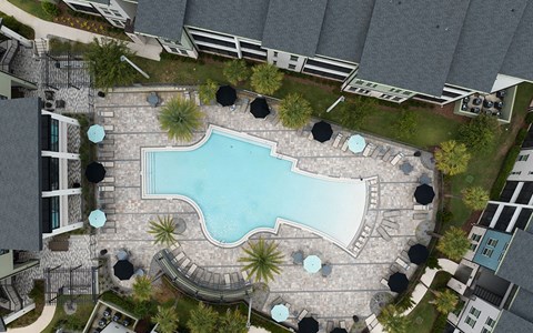 A swimming pool surrounded by a stone patio and umbrella tables.