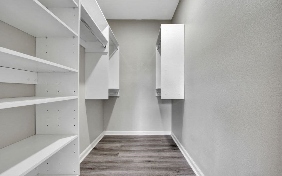 a walk in closet with white cabinets and a wooden floor