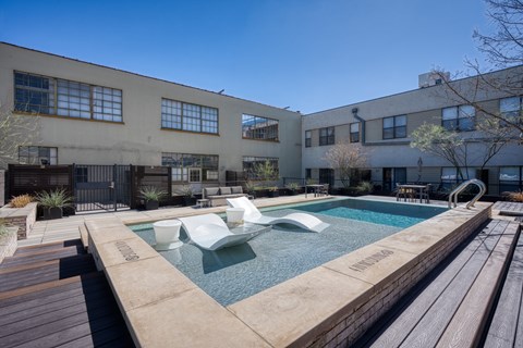 A pool with a wooden deck and a building in the background.