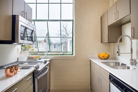 A kitchen with white cabinets and a window overlooking a house.