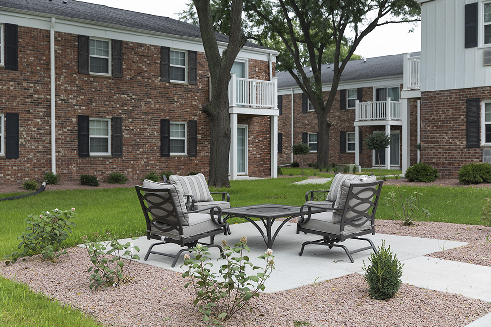 a patio with two chairs and a table in front of an apartment building