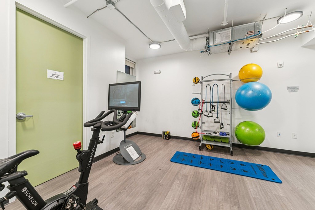 A room with a stationary bike, a TV monitor, and exercise equipment.