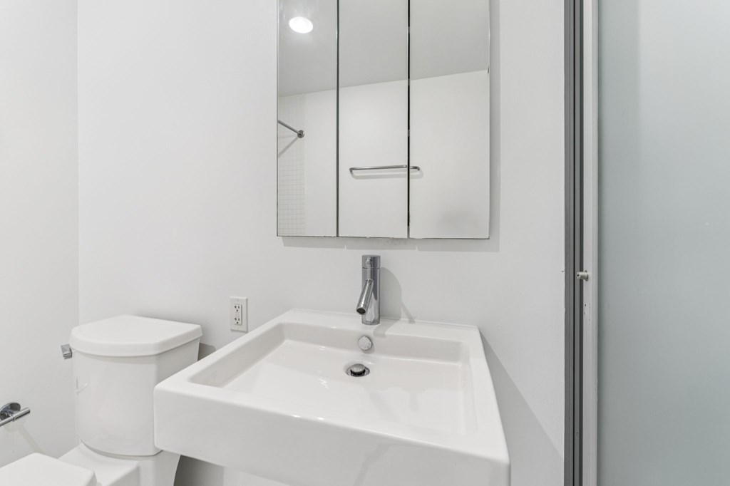 A white bathroom with a toilet, sink and mirror.