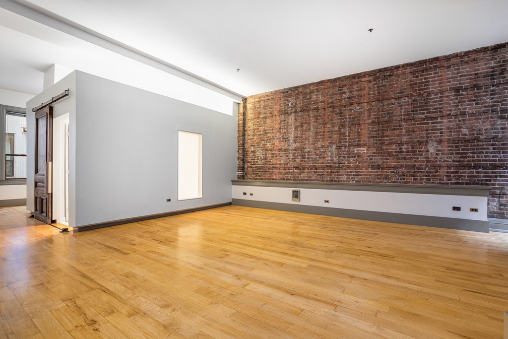 an empty living room with a brick wall and wooden floors