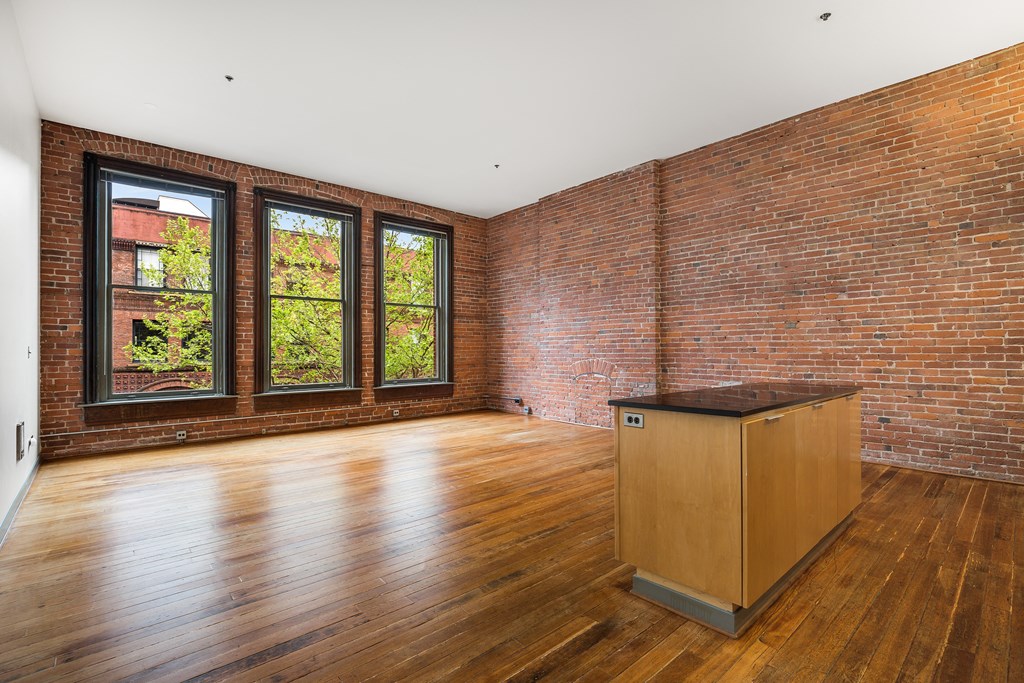 an empty living room with exposed brick walls and a wooden floor