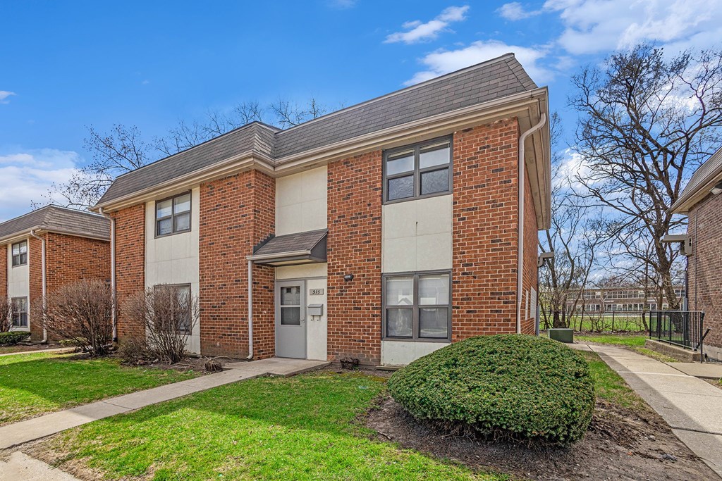 A brick apartment building with a green bush in front.