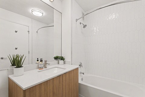 A white bathroom with a wooden vanity and a white bathtub.