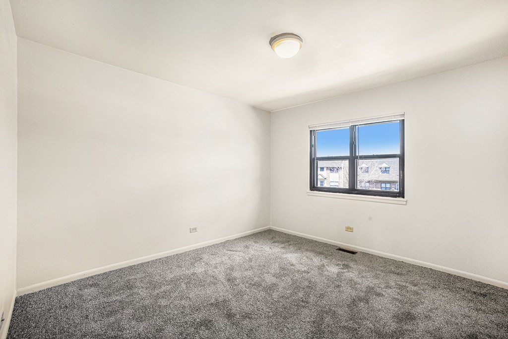A room with a window and a grey carpet.