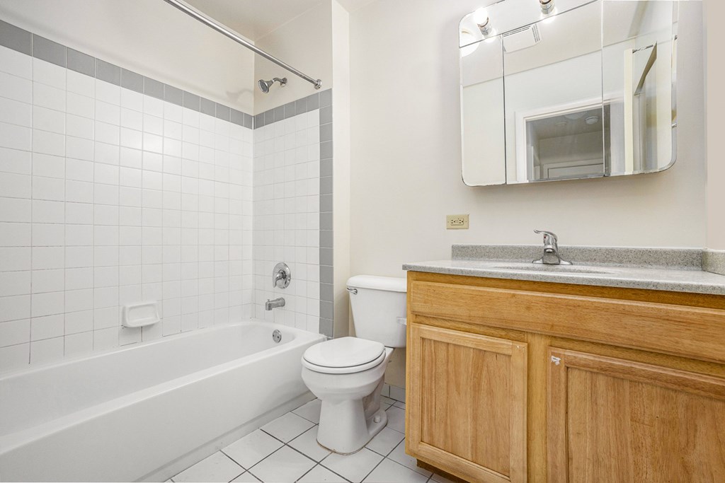 A white tiled bathroom with a wooden cabinet and a white toilet.