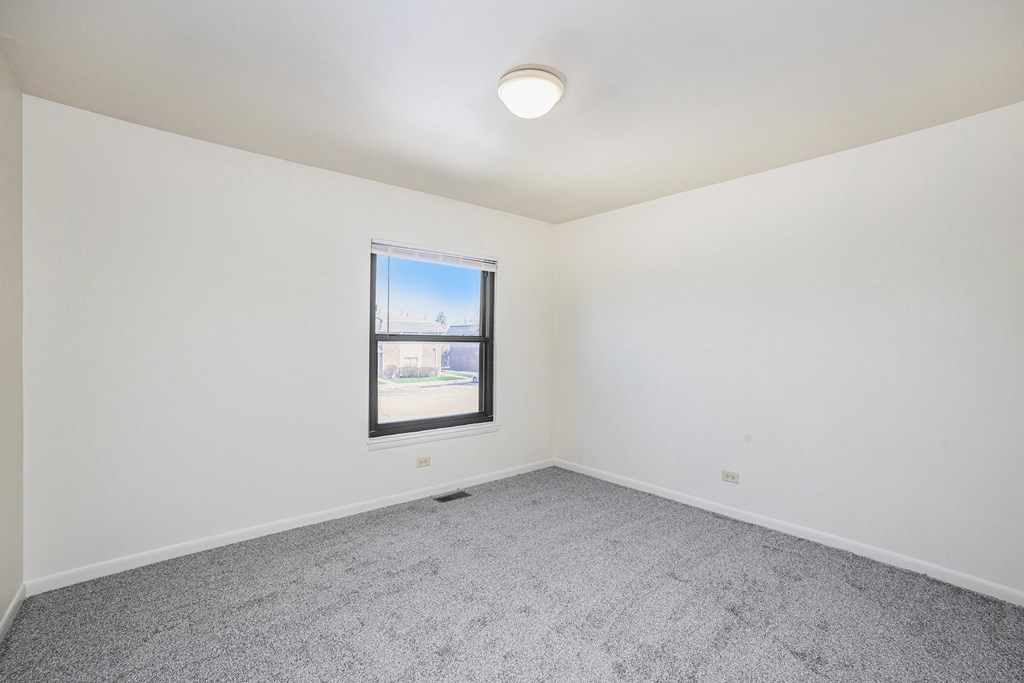 A room with a window and a grey carpet.