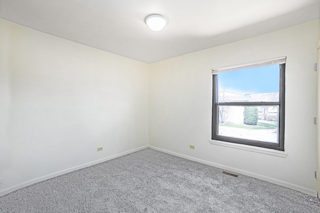 A room with a window and a grey carpet.