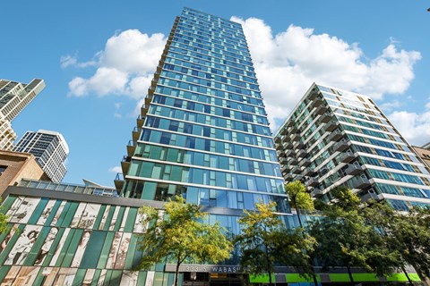 A tall glass building stands in front of other buildings and trees.