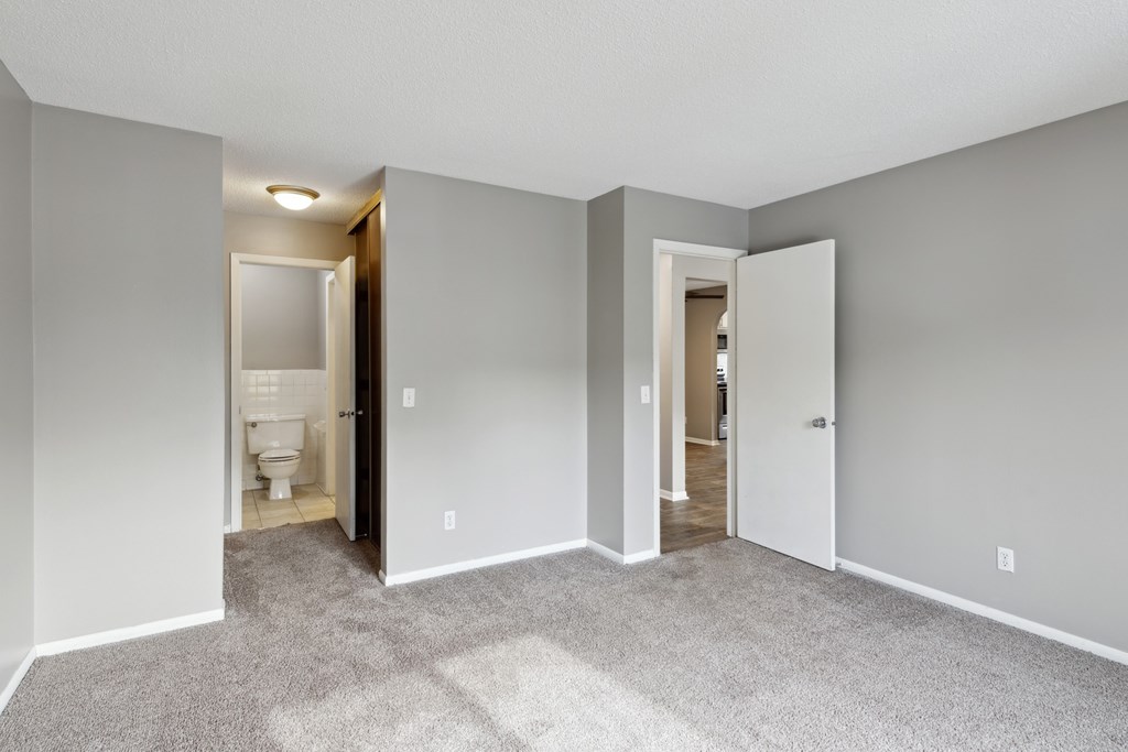 A room with carpeted floors and white walls with two open doors.